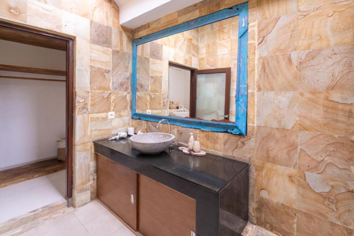 Spacious Balinese-style kitchen with intricate tiled walls, wooden cabinets, central island counter, and stainless steel appliances. - Bali Villas