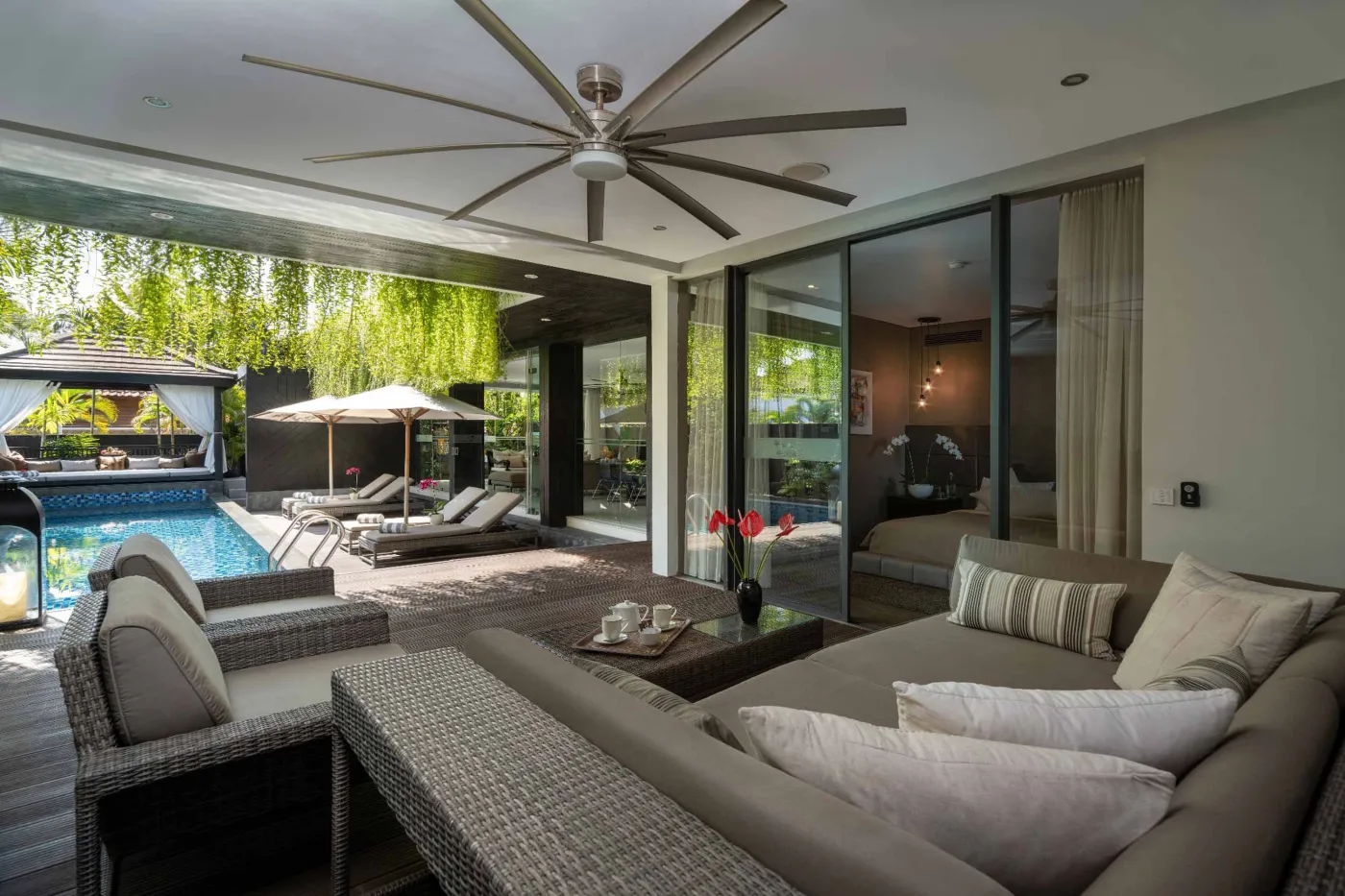 Modern dining room in a tropical villa with a set wooden table, chandelier, and glass walls overlooking a lit infinity pool and garden at night. - Bali Villas