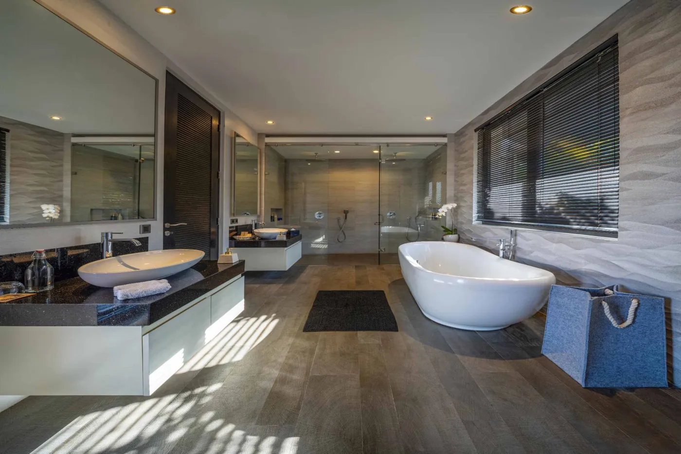 Modern dining room in a tropical villa with a set wooden table, chandelier, and glass walls overlooking a lit infinity pool and garden at night. - Bali Villas