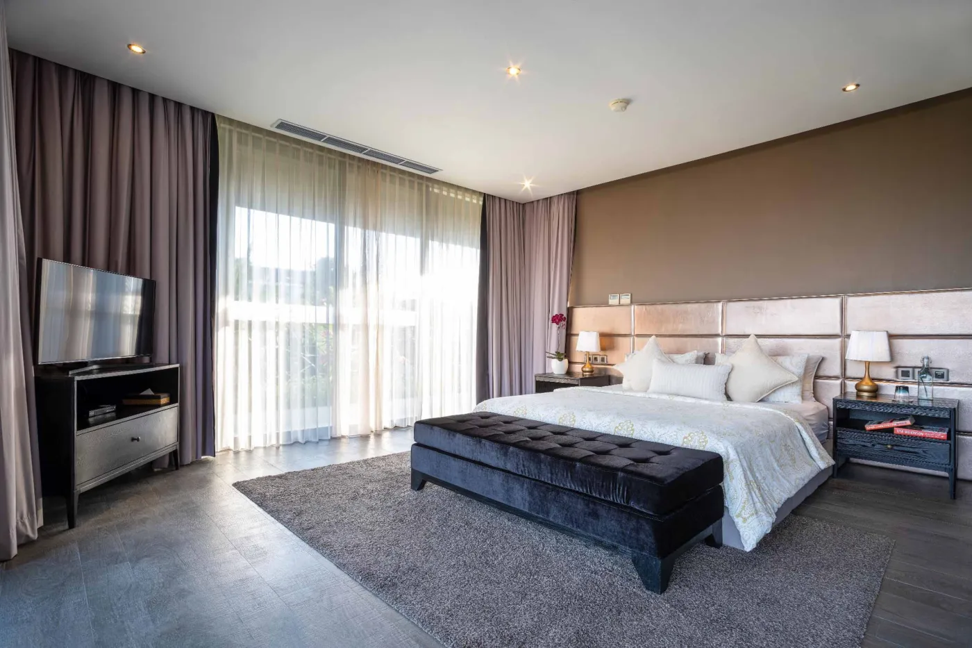 Modern dining room in a tropical villa with a set wooden table, chandelier, and glass walls overlooking a lit infinity pool and garden at night. - Bali Villas