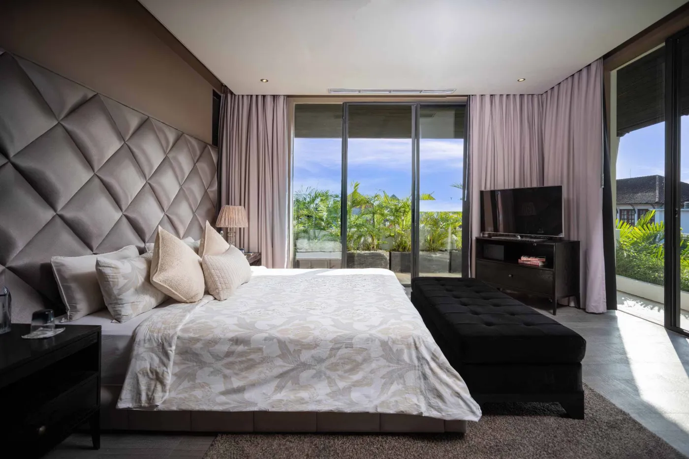 Modern dining room in a tropical villa with a set wooden table, chandelier, and glass walls overlooking a lit infinity pool and garden at night. - Bali Villas