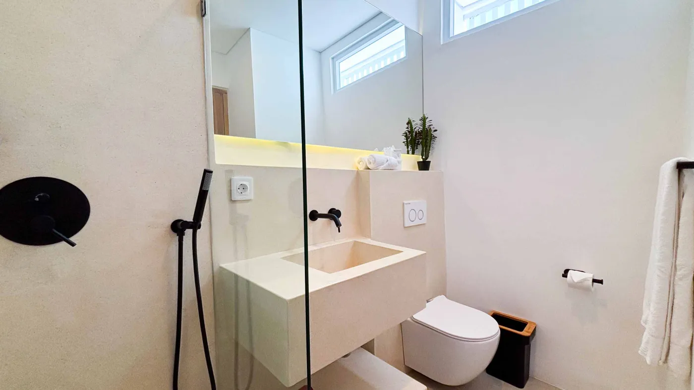 Modern minimalist bathroom with white stone sink, black fixtures, glass shower enclosure, and folded towels on counter. - Bali Villas
