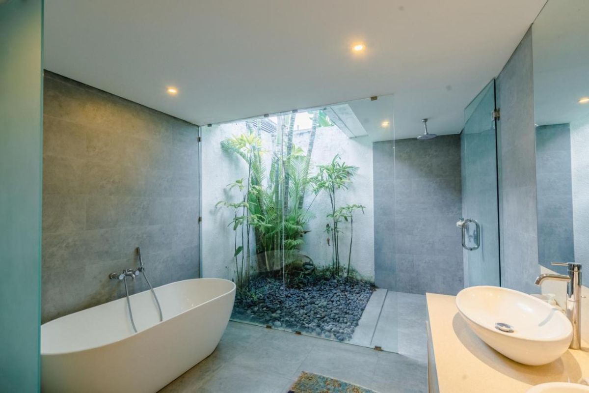 Spacious Balinese villa interior with open-plan living-dining area, wooden ceiling, wicker dining table set with colorful food, lounge sofas, and sliding doors to tropical pool garden. - Bali Villas