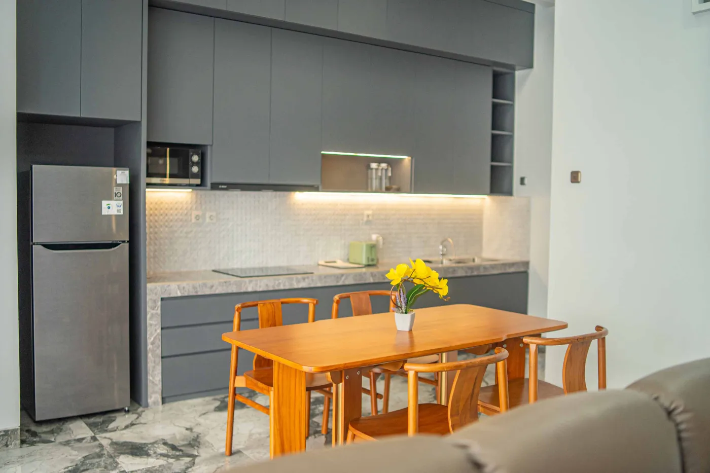 Modern living room interior with beige L-shaped sofa, wall-mounted TV, blue LED ceiling lights, textured gray wall, and potted plants. - Bali Villas