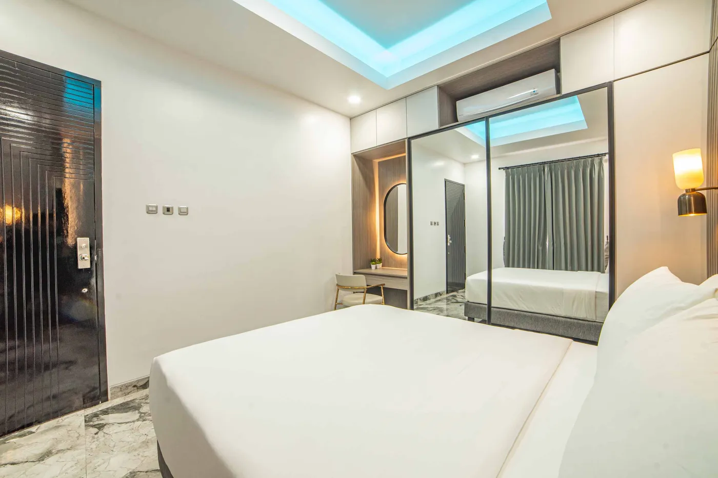 Modern living room interior with beige L-shaped sofa, wall-mounted TV, blue LED ceiling lights, textured gray wall, and potted plants. - Bali Villas