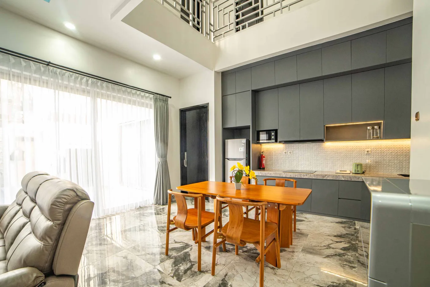 Modern living room interior with beige L-shaped sofa, wall-mounted TV, blue LED ceiling lights, textured gray wall, and potted plants. - Bali Villas
