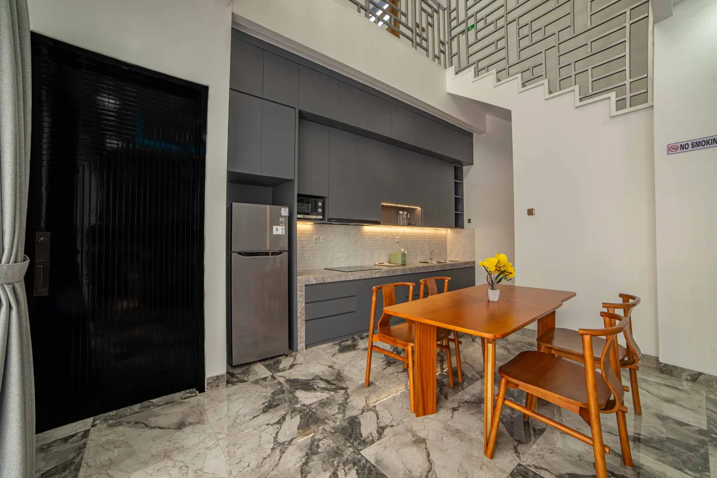 Modern living room interior with beige L-shaped sofa, wall-mounted TV, blue LED ceiling lights, textured gray wall, and potted plants. - Bali Villas