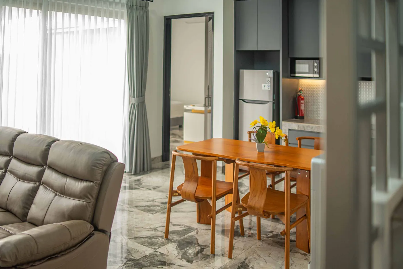 Modern living room interior with beige L-shaped sofa, wall-mounted TV, blue LED ceiling lights, textured gray wall, and potted plants. - Bali Villas