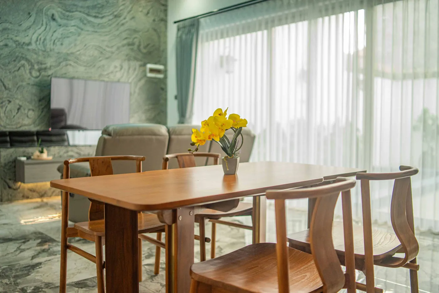 Modern living room interior with beige L-shaped sofa, wall-mounted TV, blue LED ceiling lights, textured gray wall, and potted plants. - Bali Villas