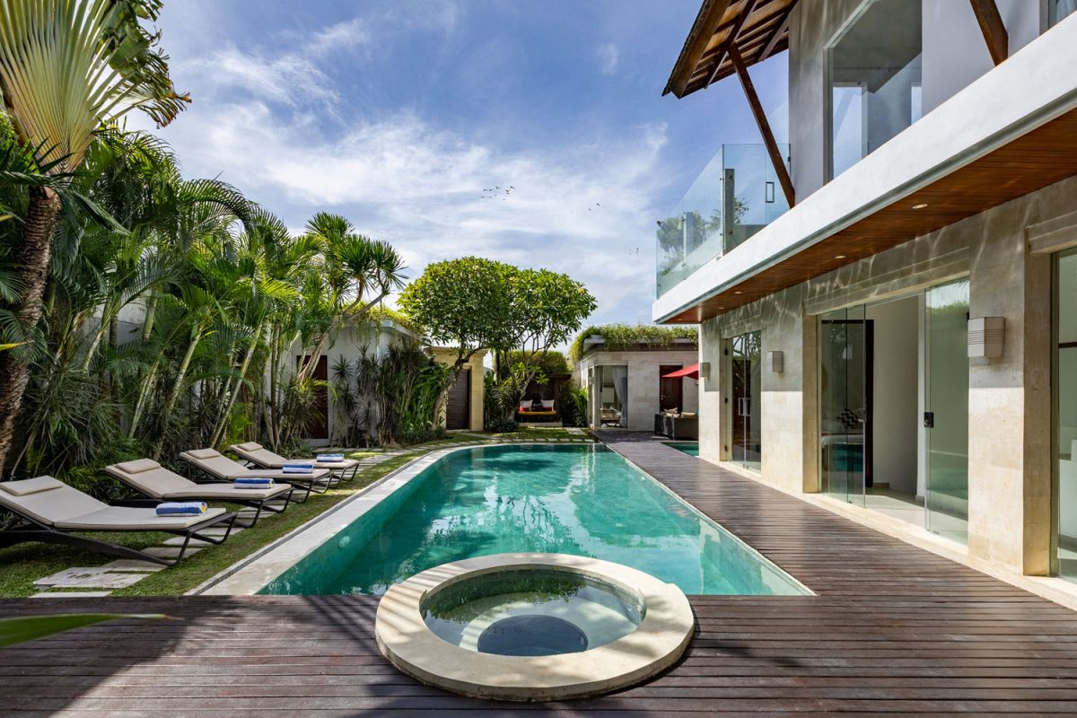 Modern Balinese kitchen interior with white cabinets, marble island, wooden bar stools, pendant lights, and tropical greenery. - Bali Villas