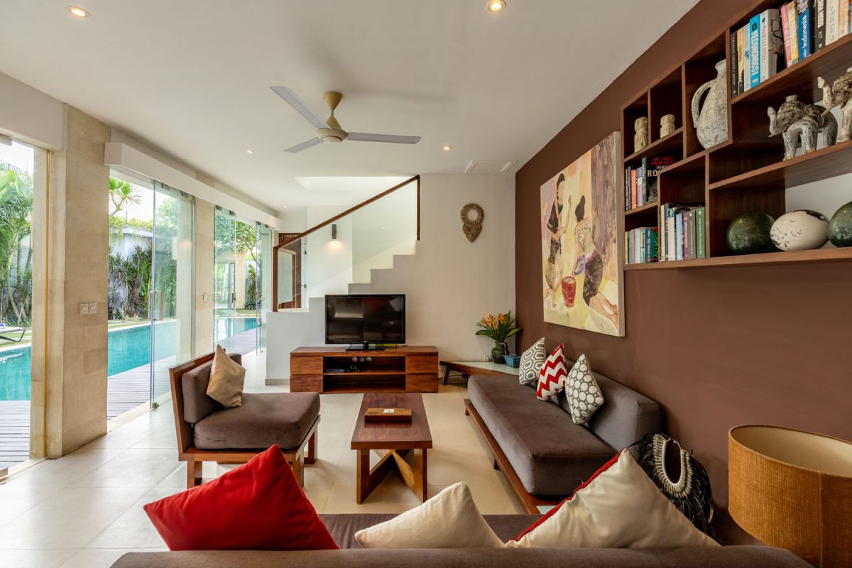 Modern Balinese kitchen interior with white cabinets, marble island, wooden bar stools, pendant lights, and tropical greenery. - Bali Villas
