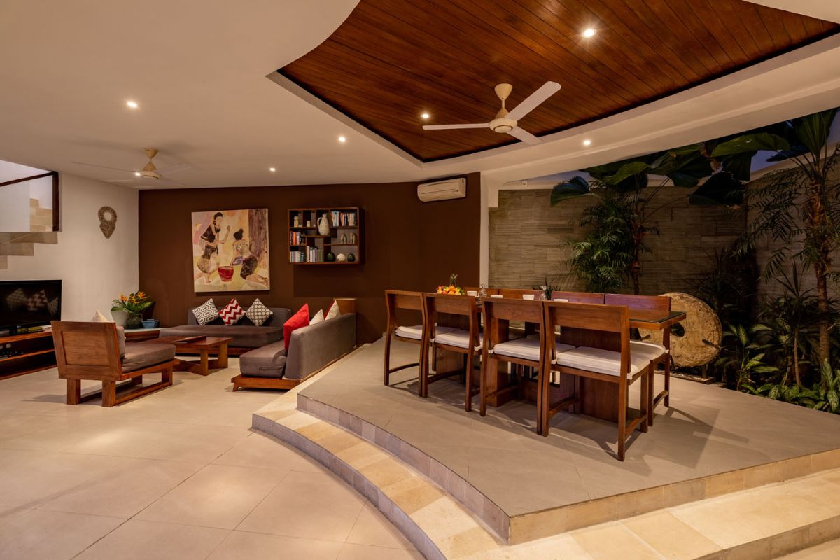 Modern Balinese kitchen interior with white cabinets, marble island, wooden bar stools, pendant lights, and tropical greenery. - Bali Villas