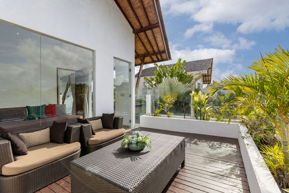 Modern Balinese kitchen interior with white cabinets, marble island, wooden bar stools, pendant lights, and tropical greenery. - Bali Villas