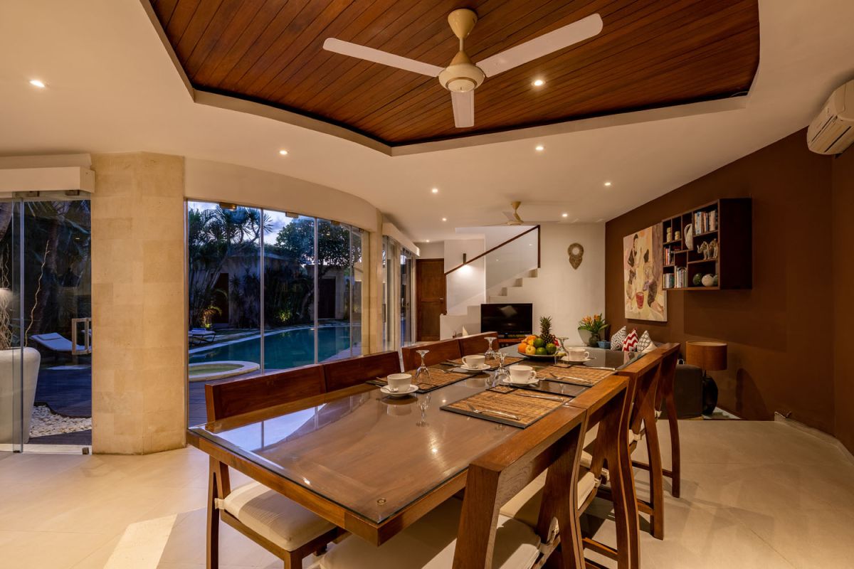 Modern Balinese kitchen interior with white cabinets, marble island, wooden bar stools, pendant lights, and tropical greenery. - Bali Villas