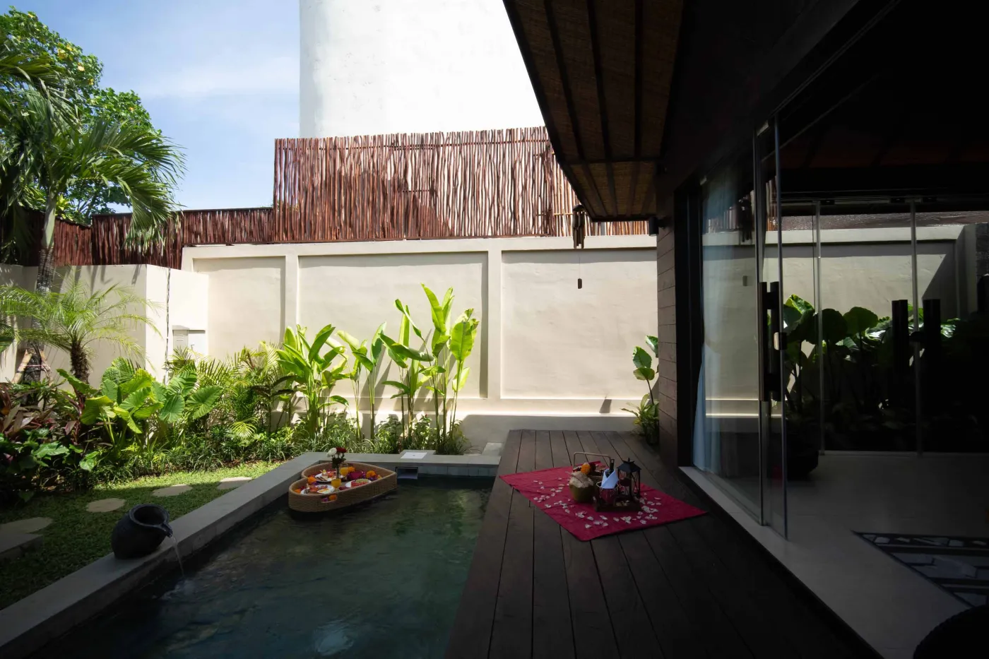Luxurious outdoor Balinese bathtub with rose petals, tropical flowers, and champagne, surrounded by stone walls, hanging batik robes, and potted plants. - Bali Villas
