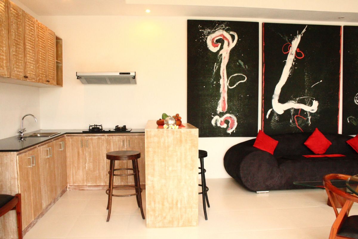 Luxurious Balinese villa interior at night: open dining area with glass table, wooden chairs, red lounger, pendant lamps, and garden pool view through white curtains. - Bali Villas