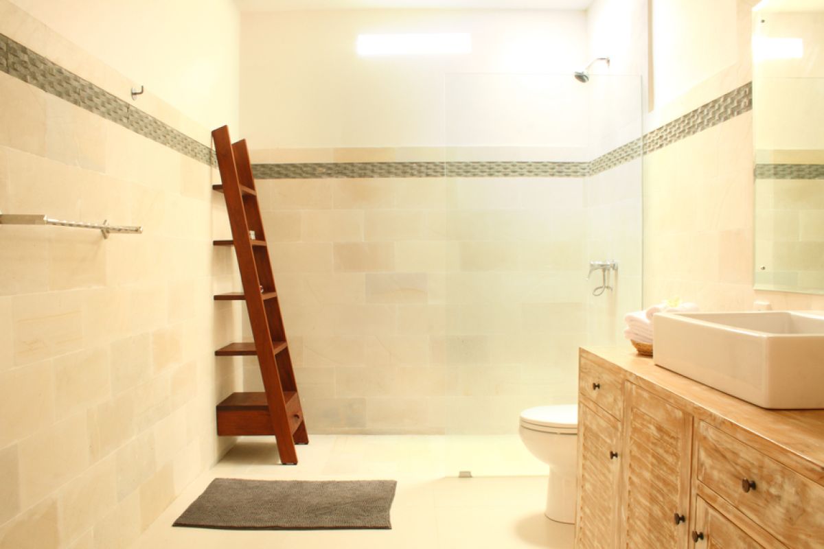 Luxurious Balinese villa interior at night: open dining area with glass table, wooden chairs, red lounger, pendant lamps, and garden pool view through white curtains. - Bali Villas