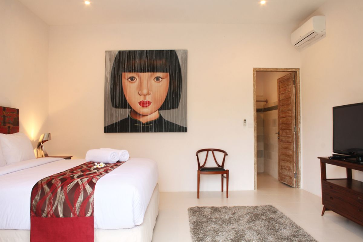 Luxurious Balinese villa interior at night: open dining area with glass table, wooden chairs, red lounger, pendant lamps, and garden pool view through white curtains. - Bali Villas