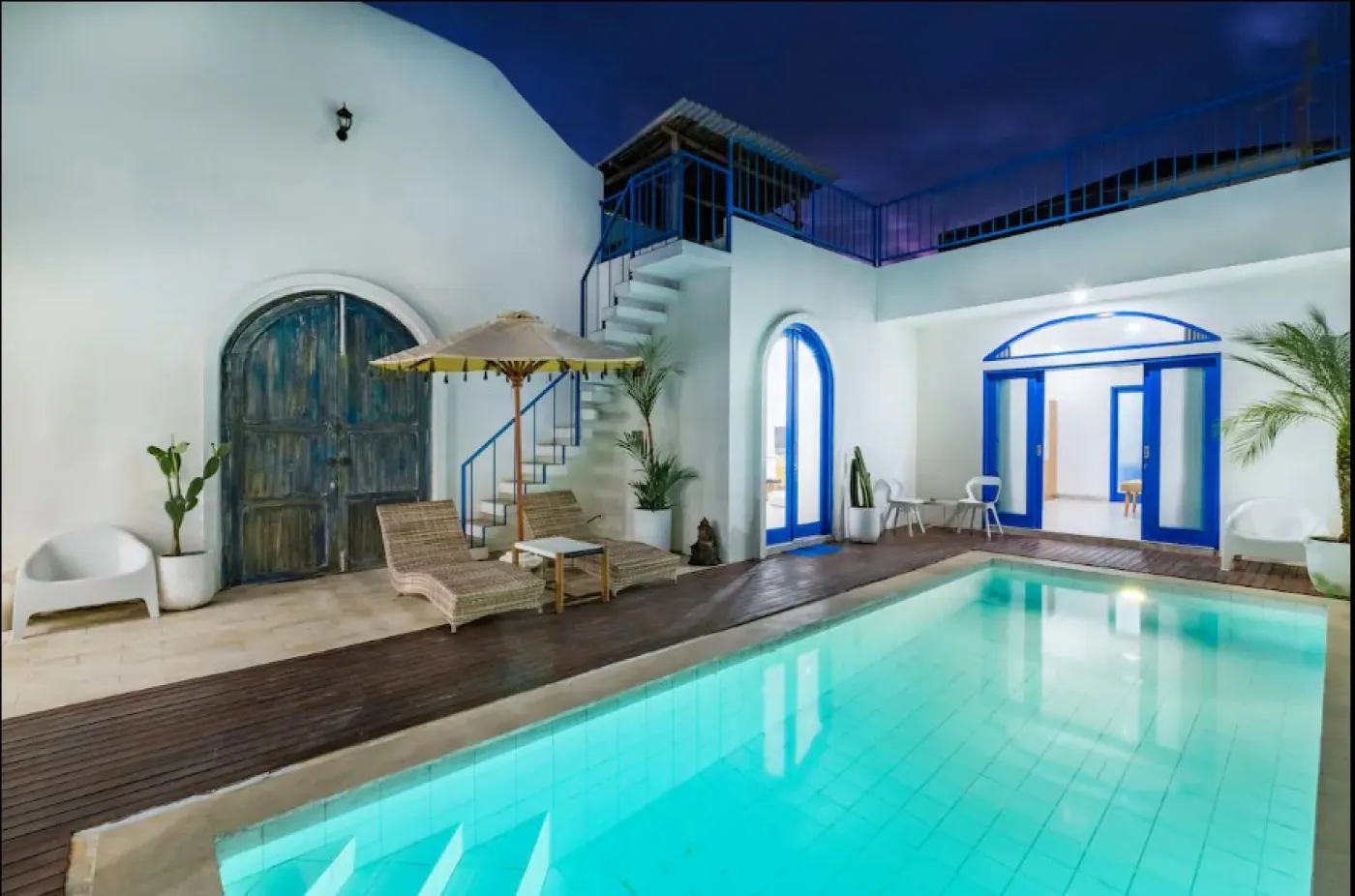 Modern open-plan tropical villa interior with white kitchen cabinets, gray sofa lounge, wooden accents, and potted plants. - Bali Villas