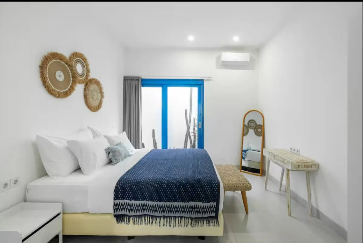 Modern open-plan tropical villa interior with white kitchen cabinets, gray sofa lounge, wooden accents, and potted plants. - Bali Villas