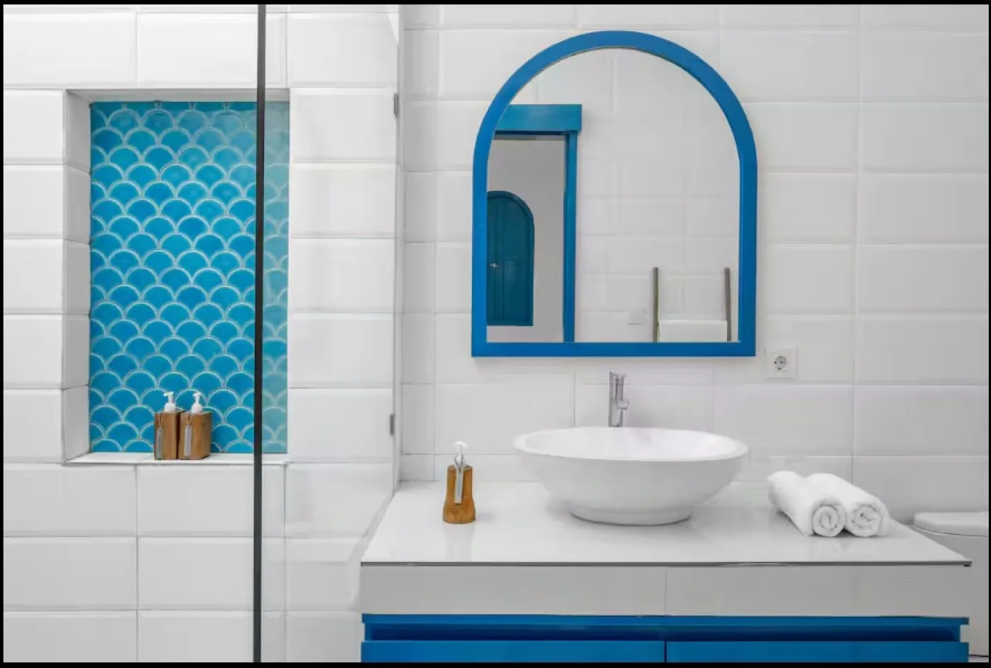 Modern open-plan tropical villa interior with white kitchen cabinets, gray sofa lounge, wooden accents, and potted plants. - Bali Villas