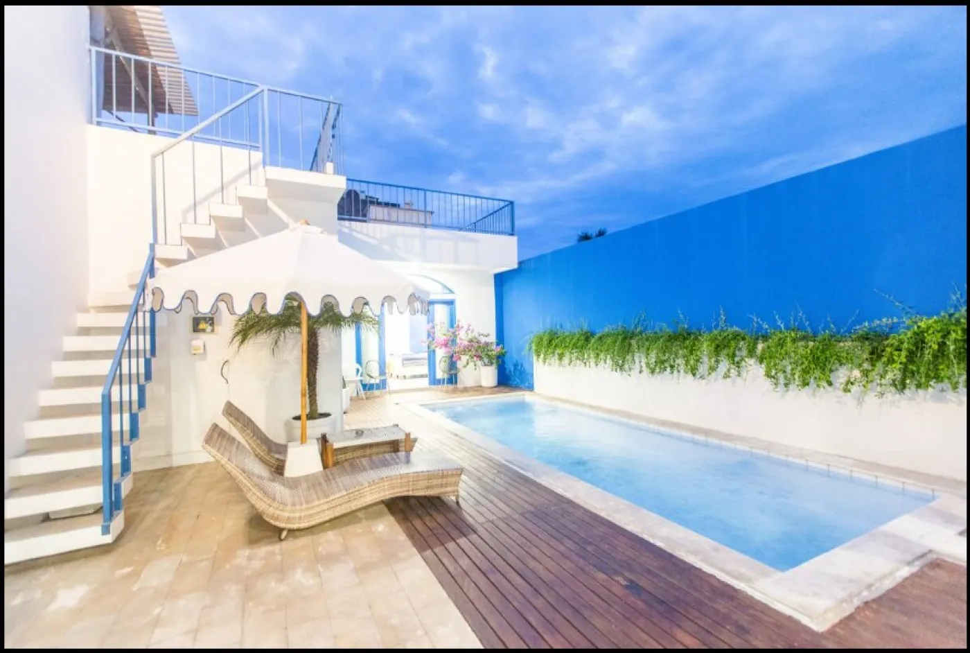 Modern open-plan tropical villa interior with white kitchen cabinets, gray sofa lounge, wooden accents, and potted plants. - Bali Villas