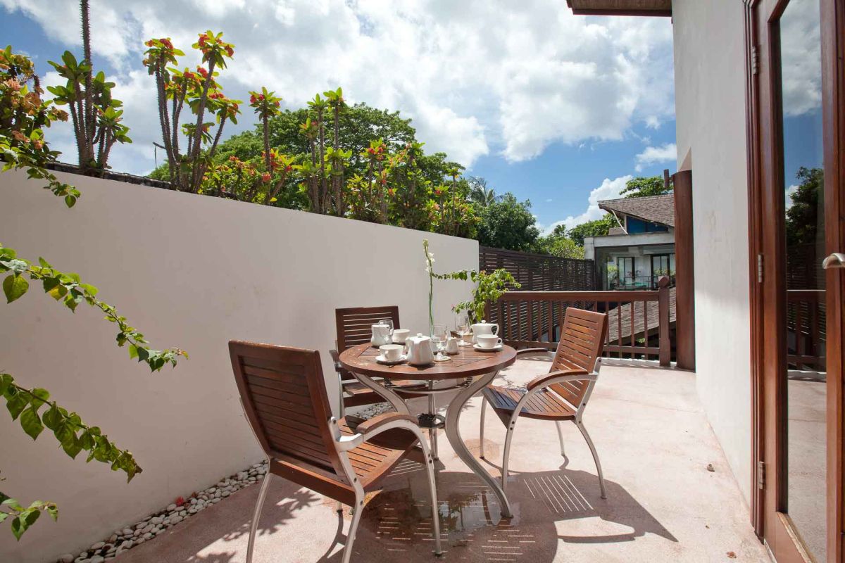 Luxurious Balinese villa rooftop terrace with green lounge chairs, white towels, potted frangipani trees, and sliding glass doors under a clear blue sky. - Bali Villas