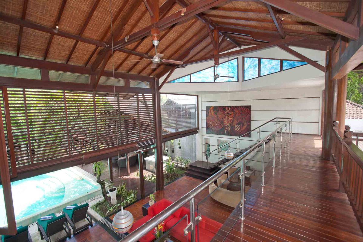 Luxurious Balinese villa rooftop terrace with green lounge chairs, white towels, potted frangipani trees, and sliding glass doors under a clear blue sky. - Bali Villas