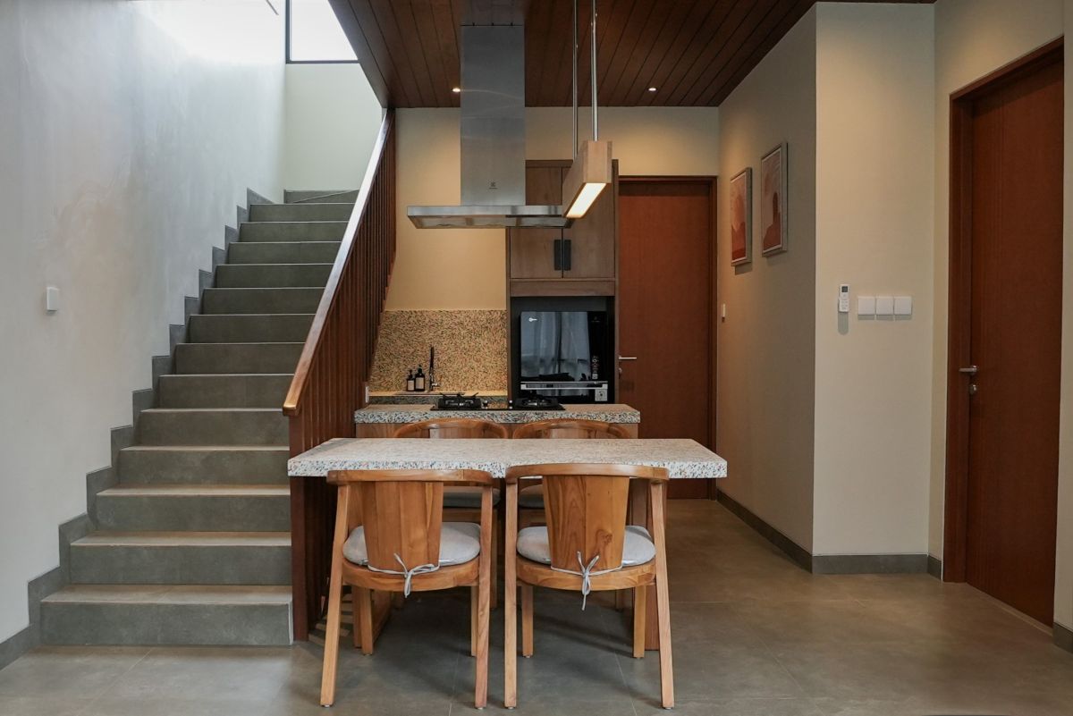 Modern open-plan kitchen with wooden island table and chairs, stainless stove, and adjacent staircase in contemporary tropical-style home. - Bali Villas