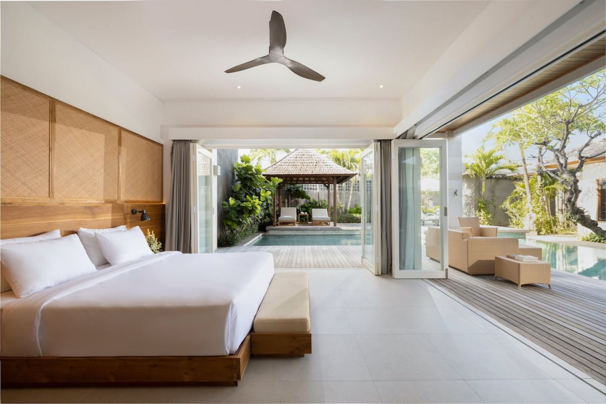 Spacious open-plan modern villa interior with wooden dining table, gray sofa, kitchen island, large garden windows, and ceiling fan. - Bali Villas