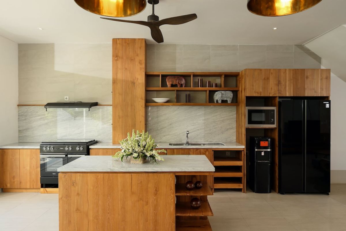 Spacious open-plan modern villa interior with wooden dining table, gray sofa, kitchen island, large garden windows, and ceiling fan. - Bali Villas