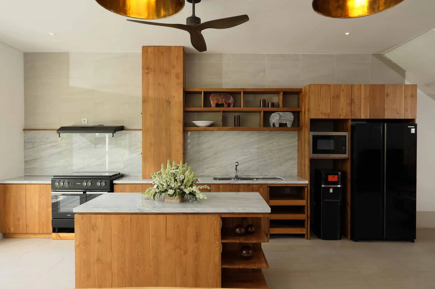 Modern wooden kitchen with marble island, black fridge, pendant lights, and tropical decor. - Bali Villas