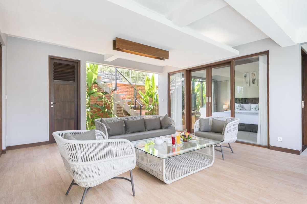 Elegant open-plan dining room in a luxury Balinese villa, featuring a glass-top table with rattan chairs, tropical centerpiece, sleek kitchen, and poolside views. - Bali Villas