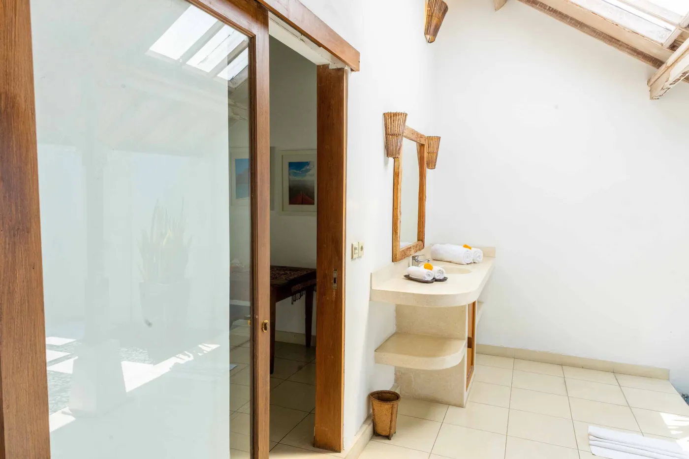 Tropical Bali-style garden with lush palms, stone pathway through green lawn, lounge chairs, blue umbrella, and circular pool beside white wall. - Bali Villas