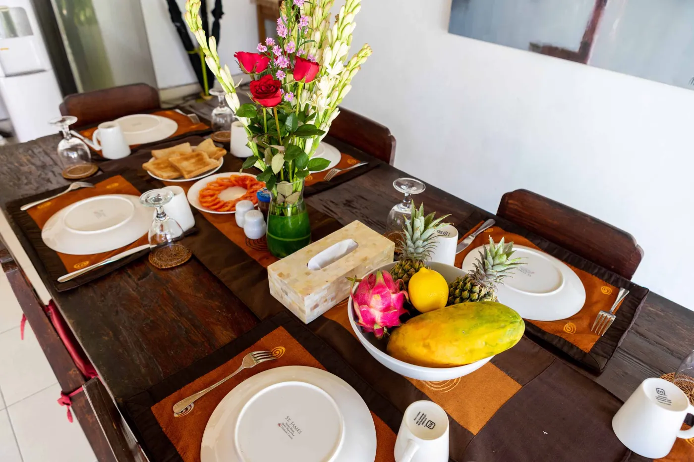 Tropical Bali-style garden with lush palms, stone pathway through green lawn, lounge chairs, blue umbrella, and circular pool beside white wall. - Bali Villas
