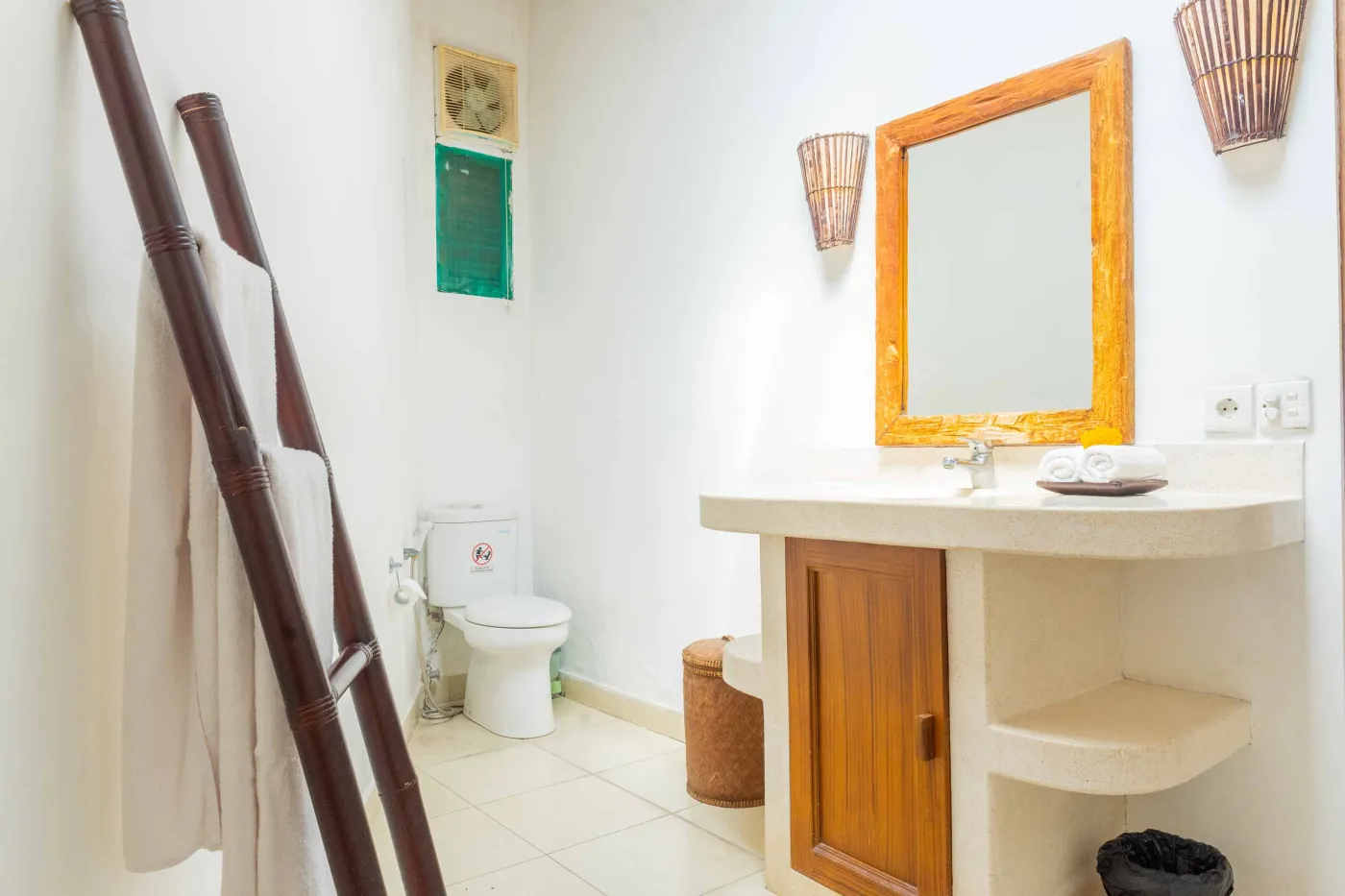 Tropical Bali-style garden with lush palms, stone pathway through green lawn, lounge chairs, blue umbrella, and circular pool beside white wall. - Bali Villas