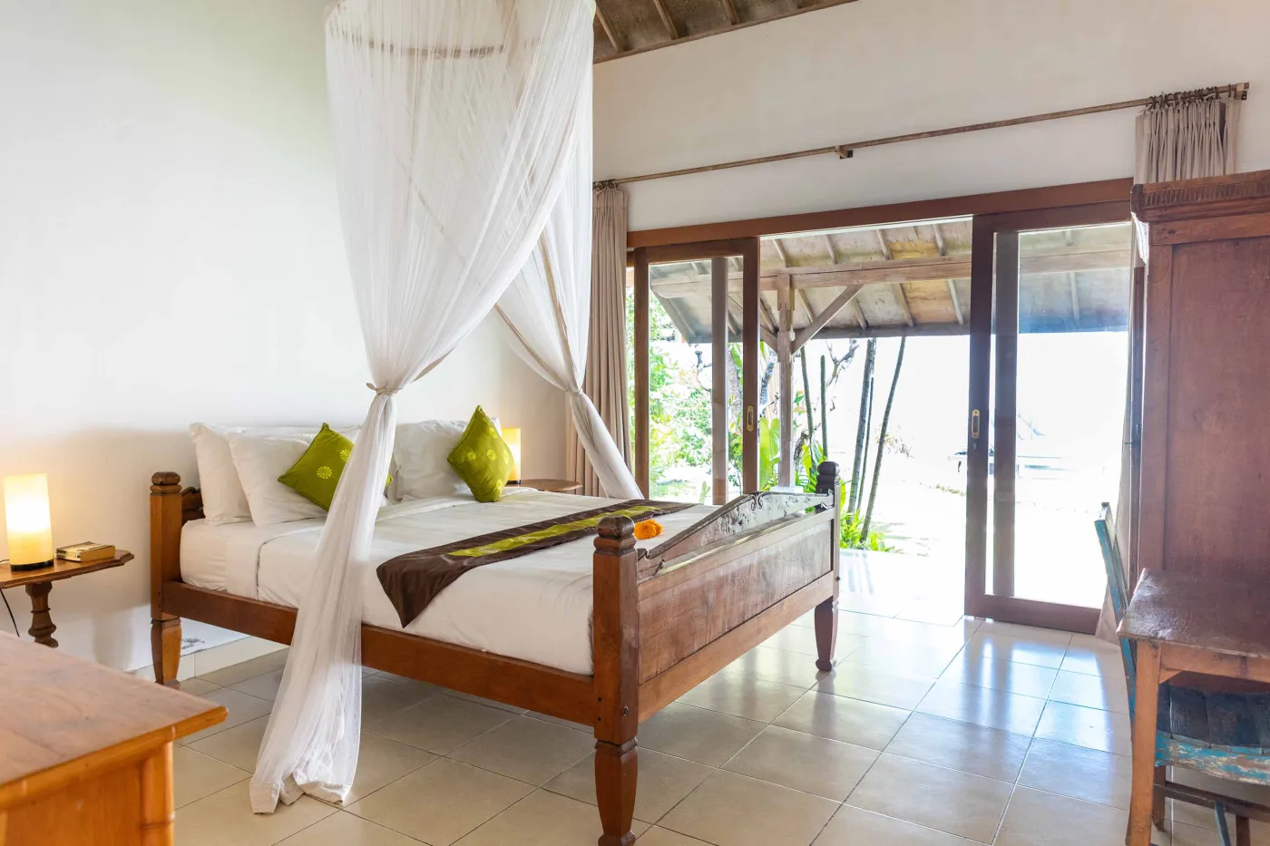 Tropical Bali-style garden with lush palms, stone pathway through green lawn, lounge chairs, blue umbrella, and circular pool beside white wall. - Bali Villas