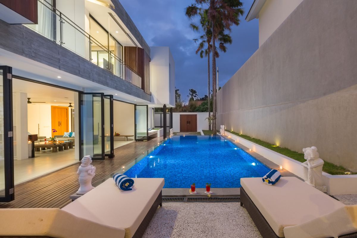 Modern white kitchen with island countertop, gas stove, stainless sink, and tropical orchid accents. - Bali Villas