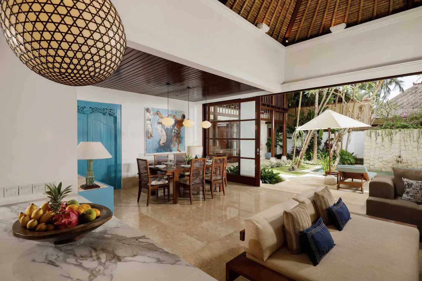 Cozy wicker chair and round table with tea set on a Balinese-style veranda, featuring thatched roof, wooden shutters, and tropical garden views. - Bali Villas