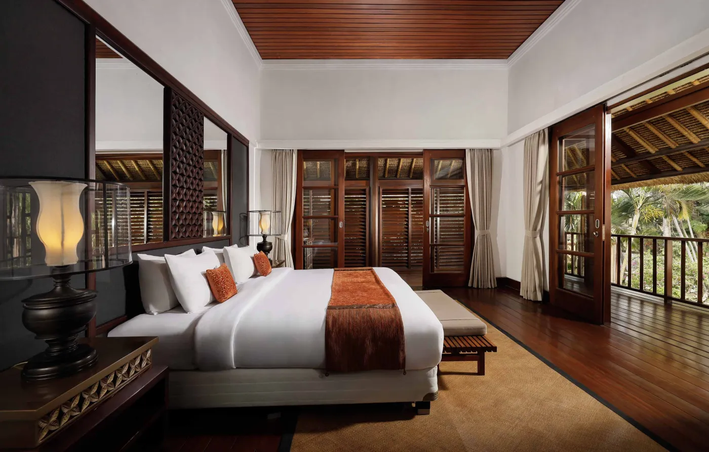 Cozy wicker chair and round table with tea set on a Balinese-style veranda, featuring thatched roof, wooden shutters, and tropical garden views. - Bali Villas