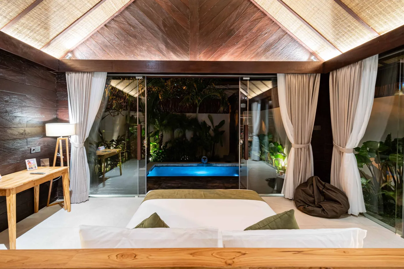 Luxurious Balinese bedroom with king bed, bamboo ceiling, lush plants, and sliding doors to private pool. - Bali Villas