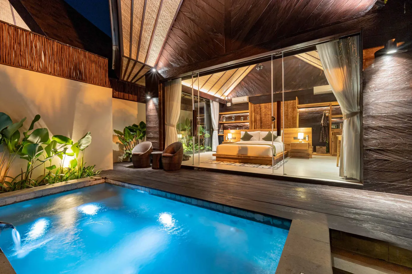 Luxurious Balinese bedroom with king bed, bamboo ceiling, lush plants, and sliding doors to private pool. - Bali Villas