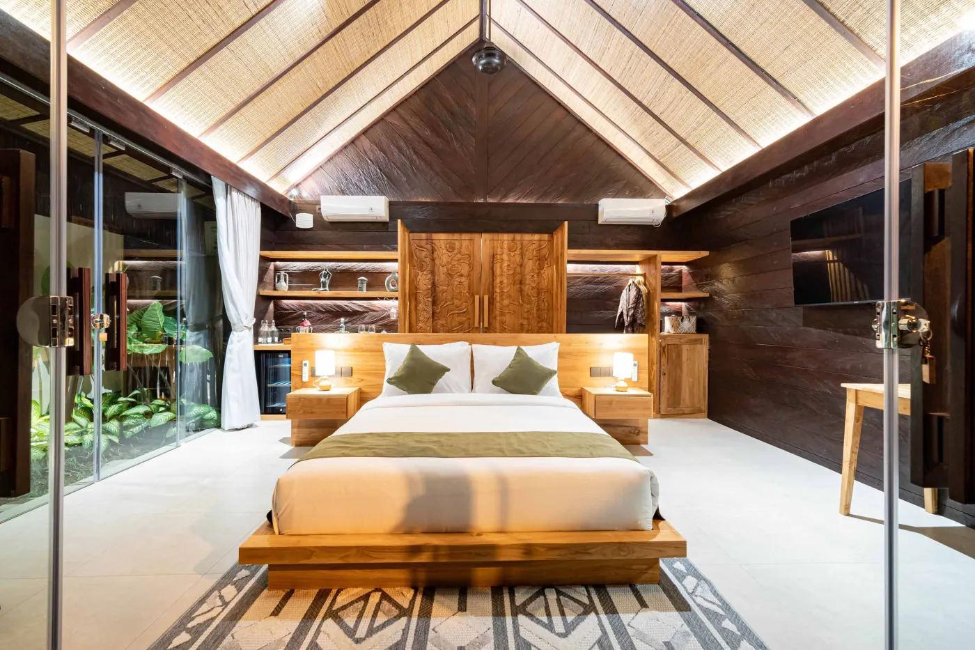 Luxurious Balinese bedroom with king bed, bamboo ceiling, lush plants, and sliding doors to private pool. - Bali Villas