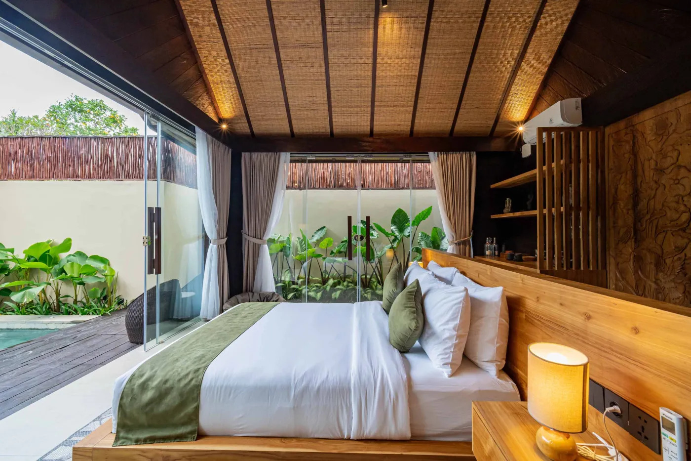 Luxurious Balinese bedroom with king bed, bamboo ceiling, lush plants, and sliding doors to private pool. - Bali Villas