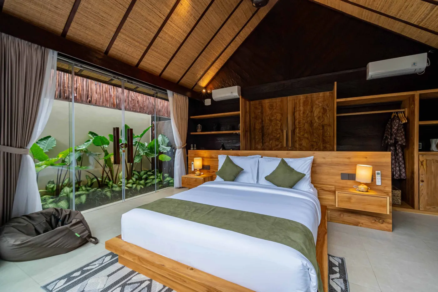 Luxurious Balinese bedroom with king bed, bamboo ceiling, lush plants, and sliding doors to private pool. - Bali Villas