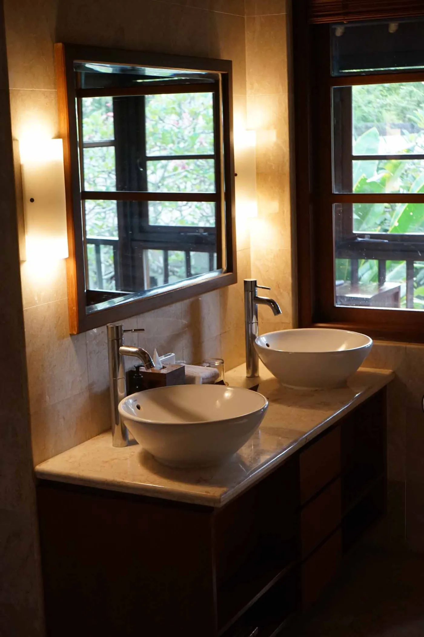 Balinese villa interior featuring a woven thatched hanging lamp, open white kitchen, and vibrant rooster wall art over a wooden dining table. - Bali Villas