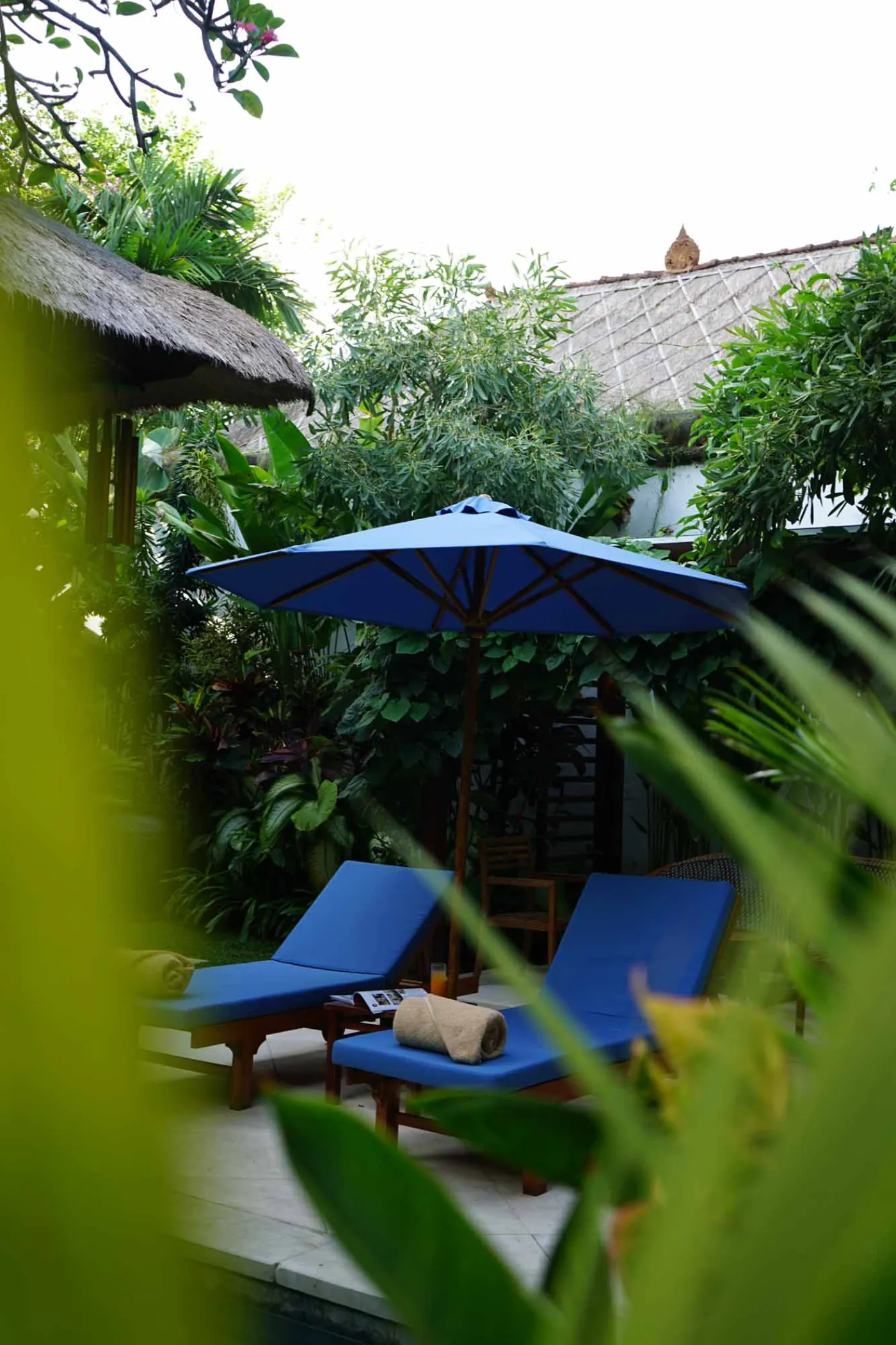 Balinese villa interior featuring a woven thatched hanging lamp, open white kitchen, and vibrant rooster wall art over a wooden dining table. - Bali Villas