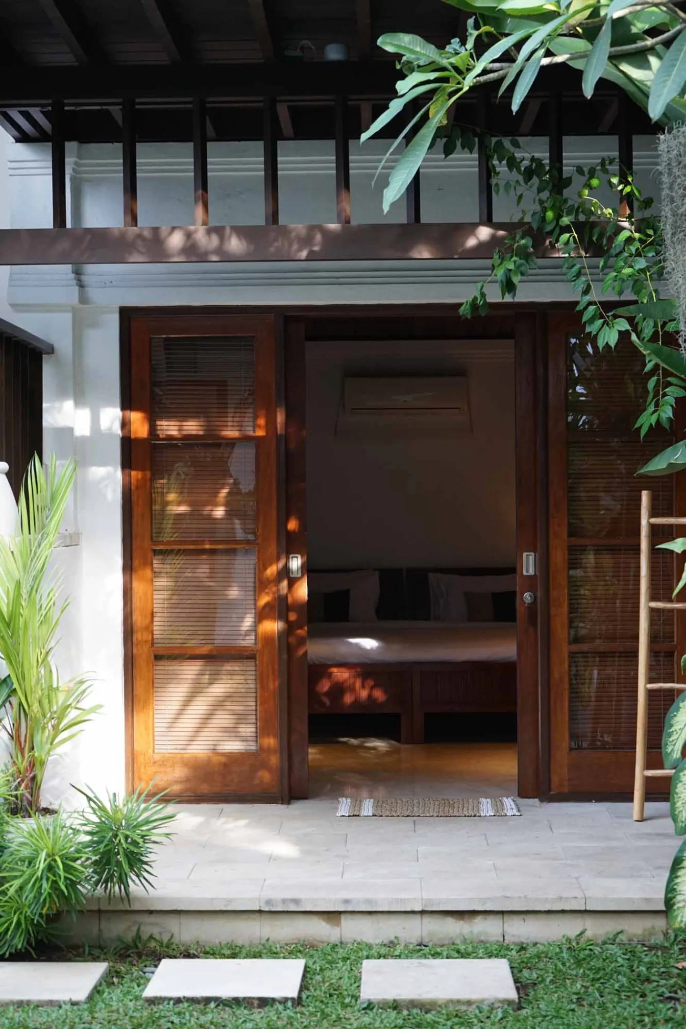Balinese villa interior featuring a woven thatched hanging lamp, open white kitchen, and vibrant rooster wall art over a wooden dining table. - Bali Villas
