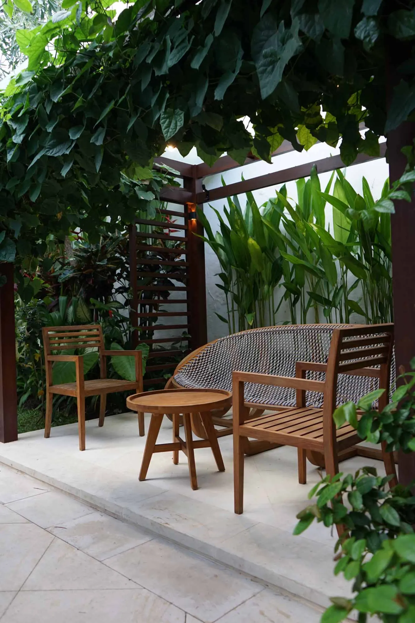 Balinese villa interior featuring a woven thatched hanging lamp, open white kitchen, and vibrant rooster wall art over a wooden dining table. - Bali Villas