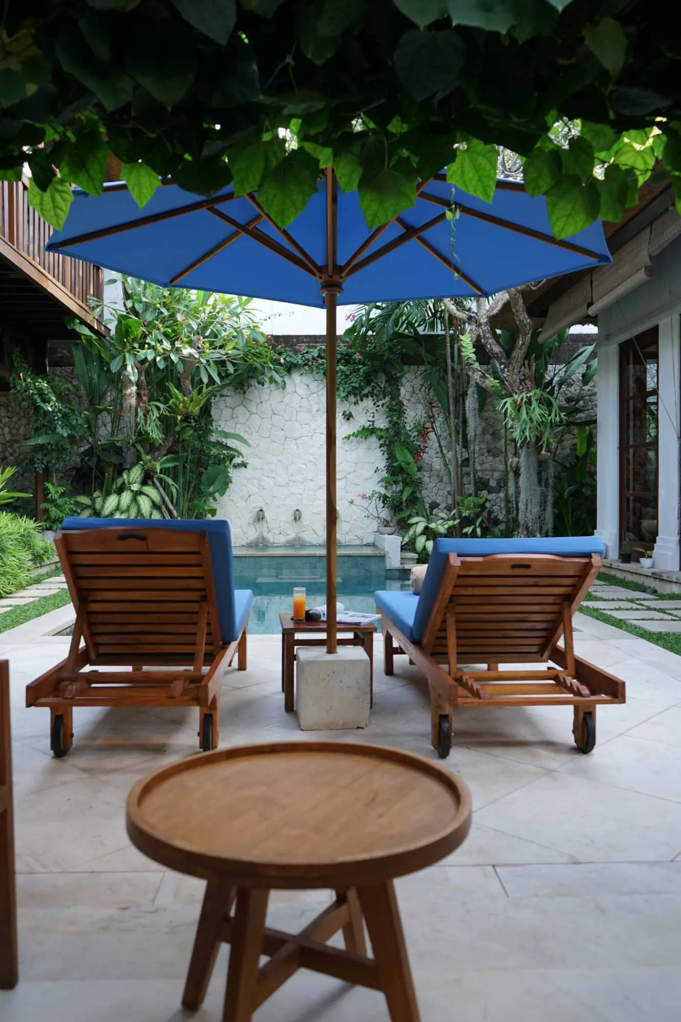 Balinese villa interior featuring a woven thatched hanging lamp, open white kitchen, and vibrant rooster wall art over a wooden dining table. - Bali Villas